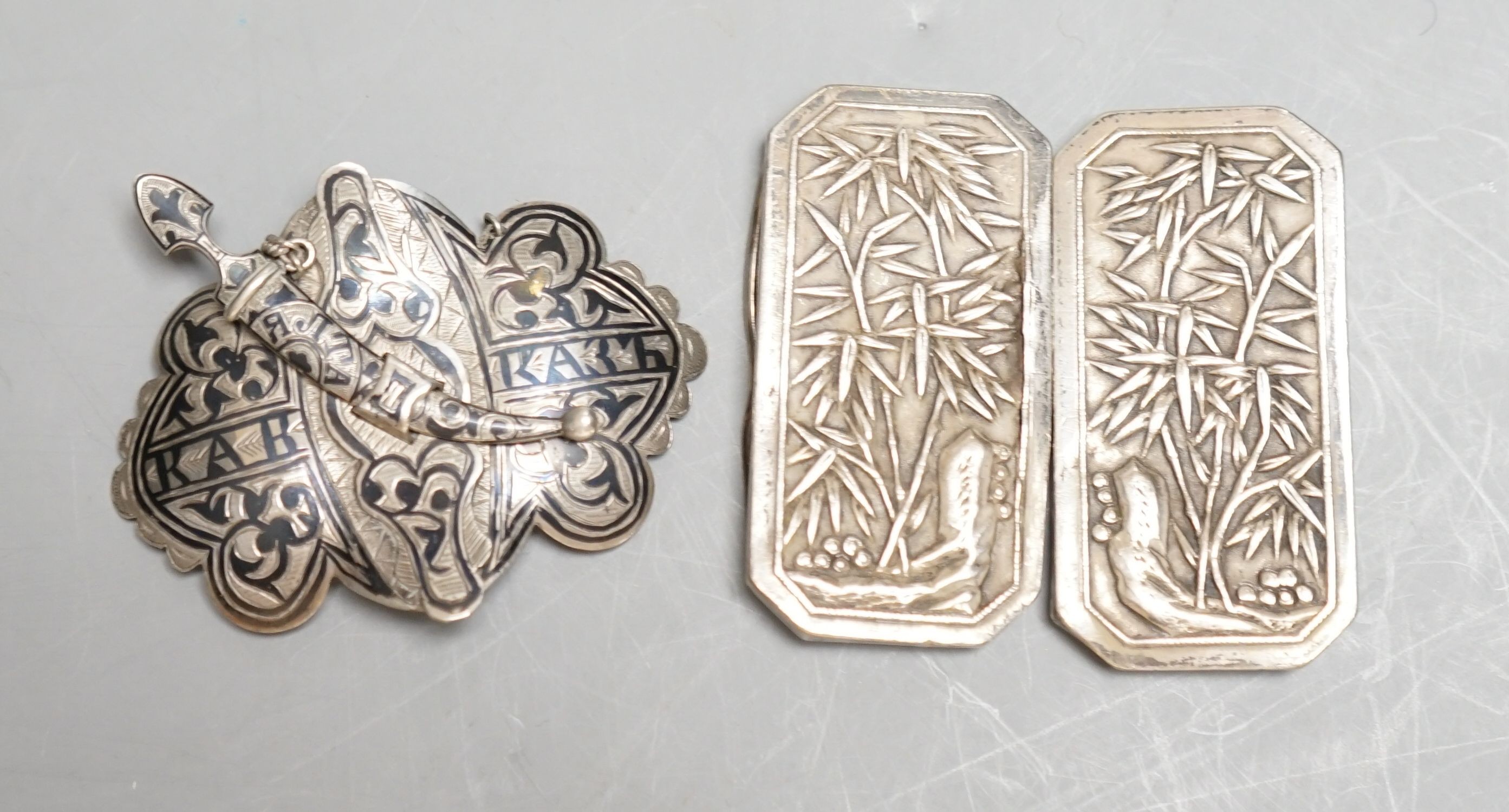 A Chinese white metal belt buckle by Wang Hing(a.f.)68mm and a Russian silver and niello work belt buckle.